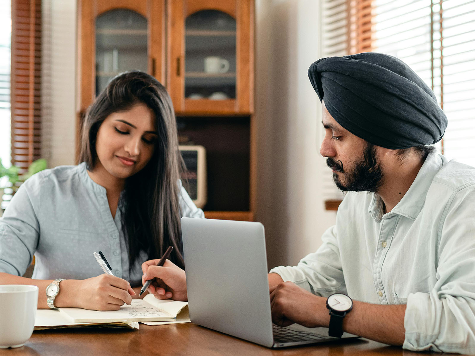 Warren UC - International Private College Consulting - How Many Schools Should I Apply to? blog post - A man and a woman sitting at a table with a laptop looking at a notebook - Pexels Ketut Subiyanto