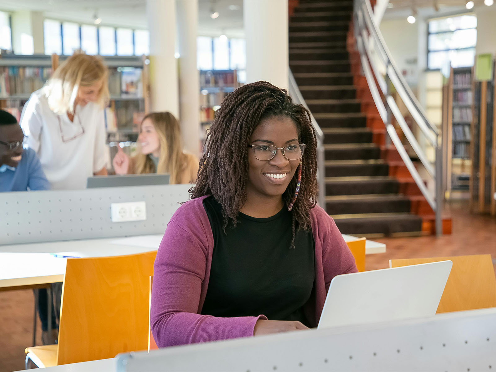 Warren UC - Private International College Consulting - How can I 'visit' a school without going there? blog post - Woman smiling at laptop in library - Pexels Kampus Production